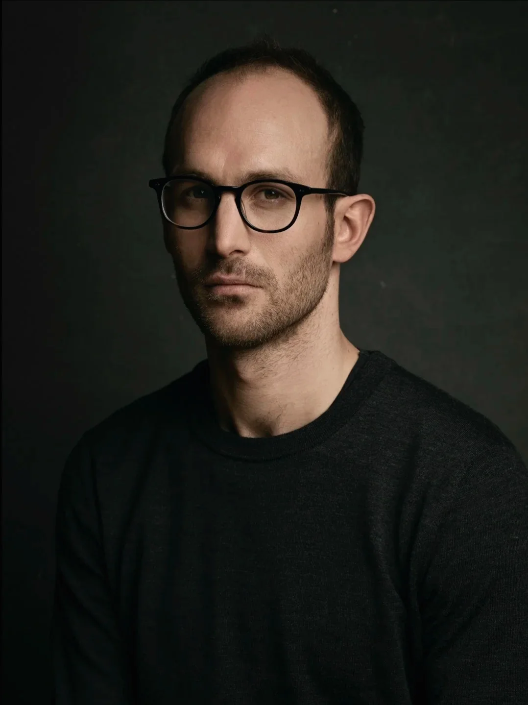Studio portrait of a man with glasses in a dark sweater.